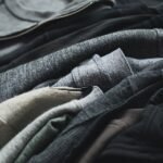Há roupas que continuam vestindo quem já não somos Stack of black and grey t-shirts and sweaters rests on a wooden table